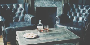 A bottle of whiskey and a glass on a table between two armchairs, a perfect whiskey gift for dad.