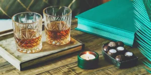 A unique bourbon gift set with two glasses, chocolates, and a gift box on a wooden tray.