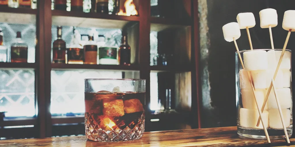 A glass of the best chocolate whiskey on ice, garnished with marshmallows.