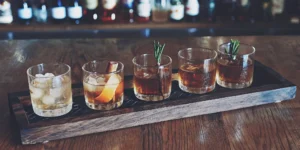 The five ways to drink whiskey presented in different glasses on a wooden tray.