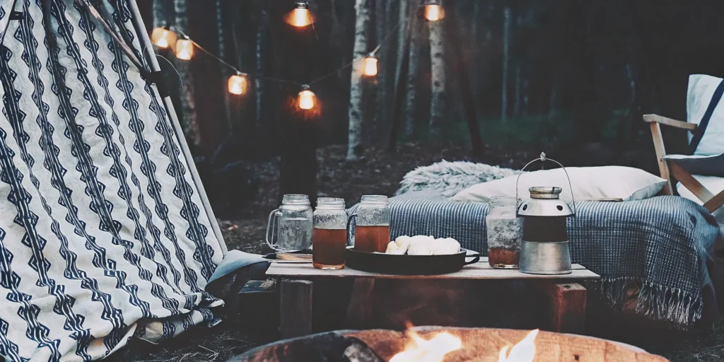 Mason jar camping drinks for adults set beside a cozy campfire with string lights.