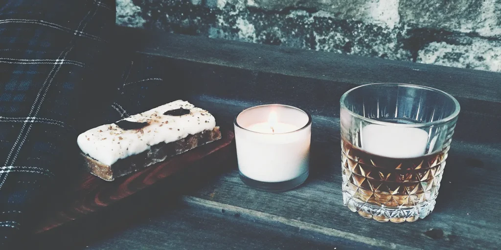 Sweet flavored whiskey in a glass next to a dessert and a lit candle.