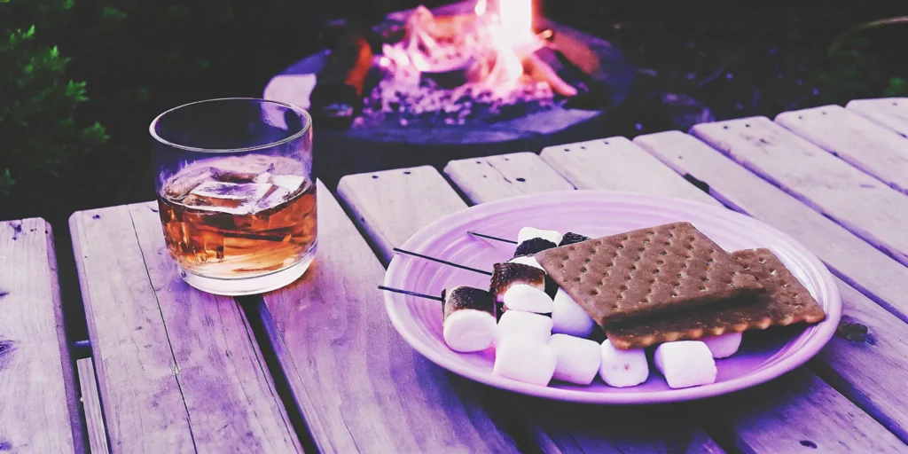 Mash and Mallow S'mores Whiskey served on ice by a campfire with toasted marshmallows.
