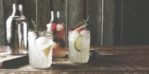 Easy make-ahead camping cocktails in mason jars with fresh fruit and herbs on a rustic table.