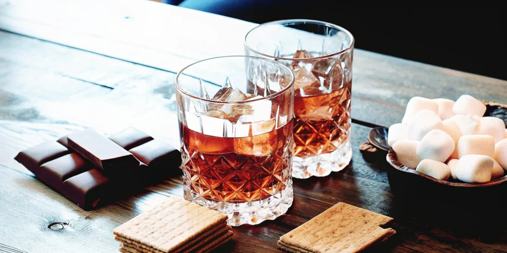 Two glasses of the best s'mores flavored alcohol, garnished with marshmallows and graham crackers.