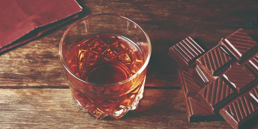 A glass of popular chocolate whiskey served on ice with pieces of dark chocolate.