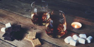 Two glasses of sweet American whiskey with chocolate, graham crackers, and marshmallows.