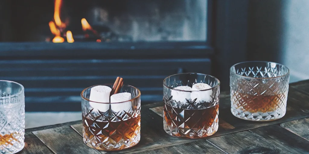 After dinner whiskey drinks with marshmallow and cinnamon garnishes by a cozy fireplace.