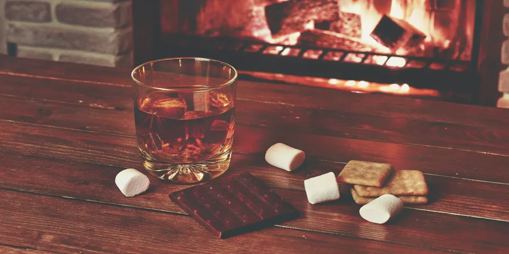 Glass of Mash & Mallow whiskey with s’mores by a fireplace, ready for whiskey delivery.