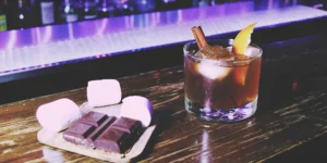 A chocolate whiskey old fashioned with an orange peel, chocolate, and marshmallow garnish.
