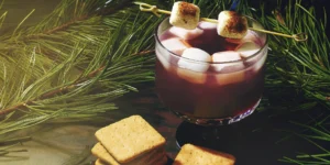 A s'mores old fashioned cocktail with a toasted marshmallow and graham cracker garnish.