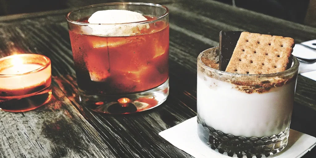 A S'mores Old Fashioned cocktail with a toasted marshmallow and graham cracker garnish.
