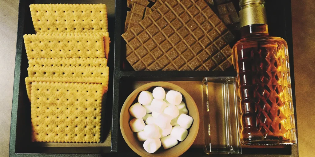 Graham cracker, chocolate, and marshmallow displayed with a bottle of s'mores whiskey.