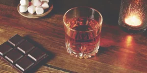 S'mores whiskey poured in a glass, surrounded by chocolate and marshmallow ingredients.