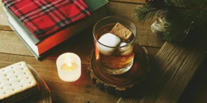 A glass of Mash & Mallow whiskey with ice and a graham cracker.