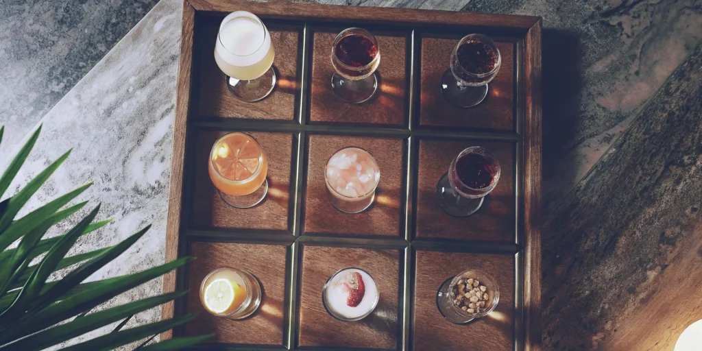A variety of interesting flavored liquors in tasting glasses on a wooden tray.