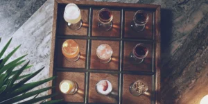 A variety of interesting flavored liquors in tasting glasses on a wooden tray.