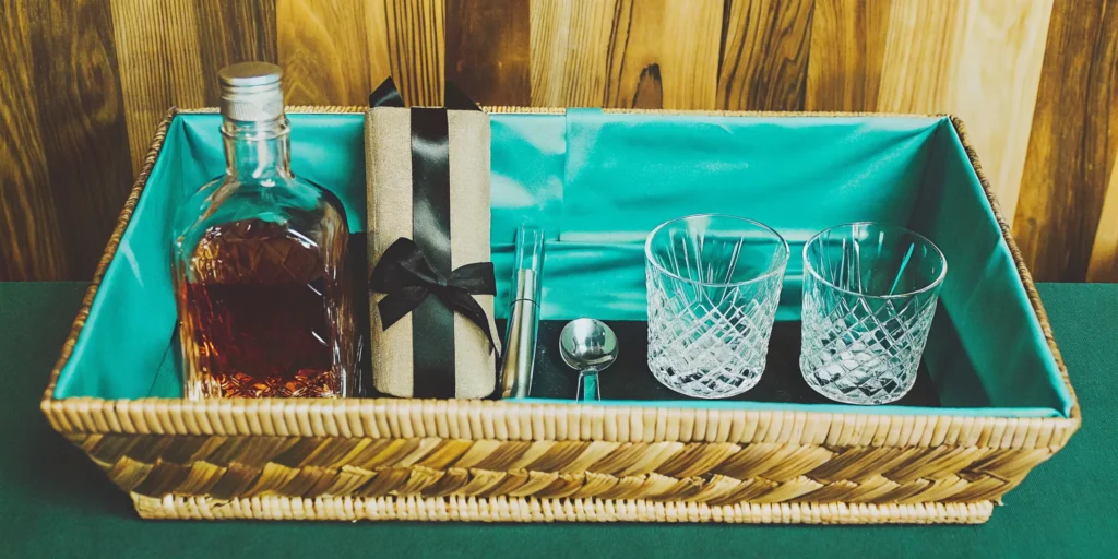 Creative bourbon gift basket idea with a bottle of whiskey, glasses, and bar tools.