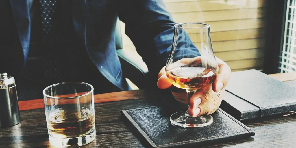 A man demonstrating the proper way to sip whiskey from a glass.