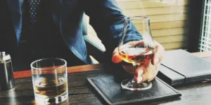 A man demonstrating the proper way to sip whiskey from a glass.
