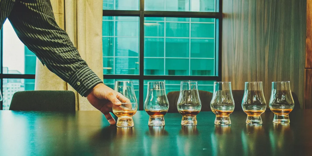 A person learning how to taste scotch with a flight of Glencairn glasses.