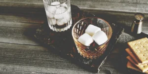 A glass of s'mores whiskey on the rocks with marshmallows and graham crackers.