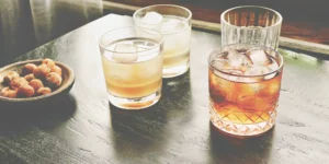 A whiskey and glass set with several drinks poured in tumblers over ice.