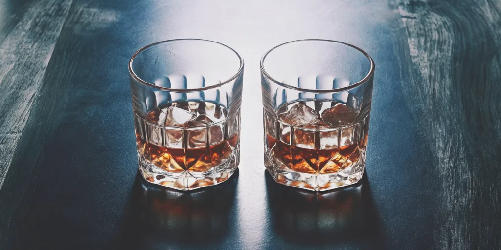 Whiskey chilled with ice cubes in one glass and with whiskey stones in another.