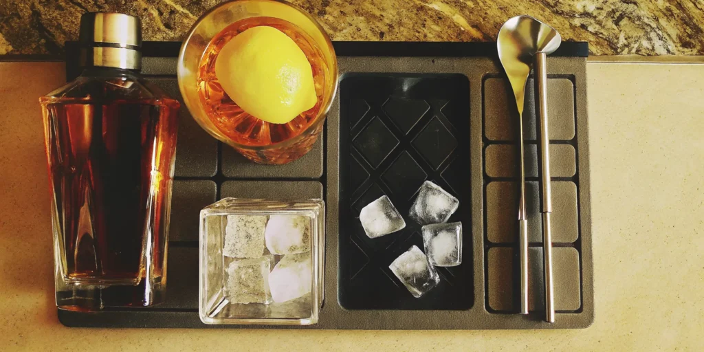 Bar setup showing how to mix a bourbon cocktail with a shaker and lemon garnish.