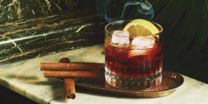 Cinnamon whiskey cocktail recipe with ice, a lemon slice, and cinnamon sticks.