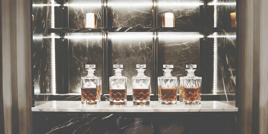 Five crystal decanters of whiskey ready for making batch cocktail recipes.