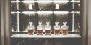 Five crystal decanters of whiskey ready for making batch cocktail recipes.